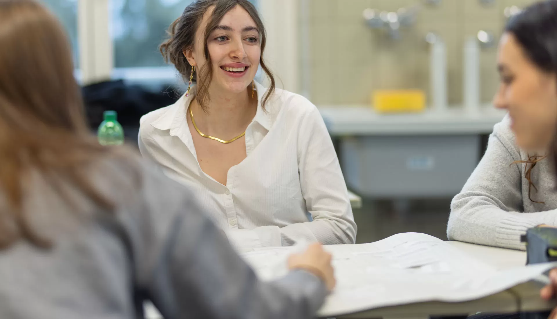 Lernende arbeiten gemeinsam am Tisch und unterhalten sich; eine Person in der Mitte lächelt.