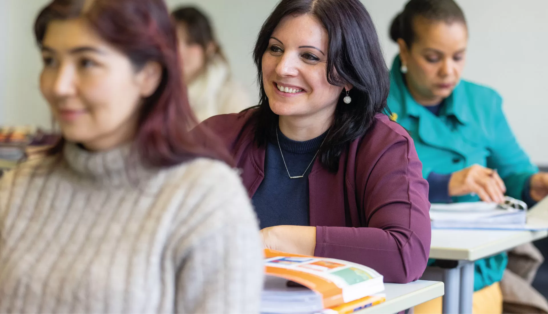 Lernende lächelt im Unterricht; im Vorder- und Hintergrund weitere Personen beim Lernen.