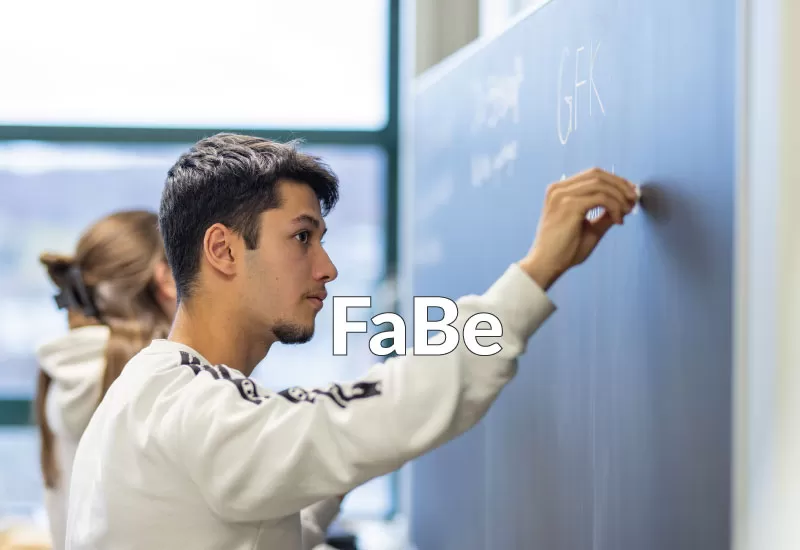 Ein junger Mann schreibt konzentriert an die Wandtafel im FaBe-Unterricht.